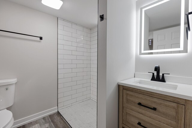 bathroom featuring toilet, a tile shower, vanity, wood finished floors, and baseboards