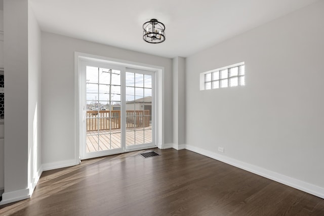 unfurnished room featuring dark wood-type flooring, visible vents, and baseboards