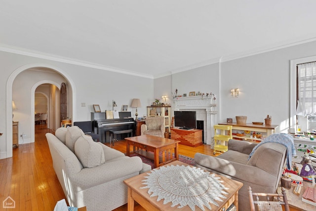 living area with light wood-style flooring, a fireplace, arched walkways, and crown molding