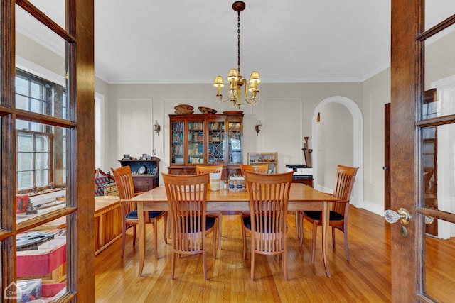 dining room with arched walkways, a notable chandelier, wood finished floors, and crown molding