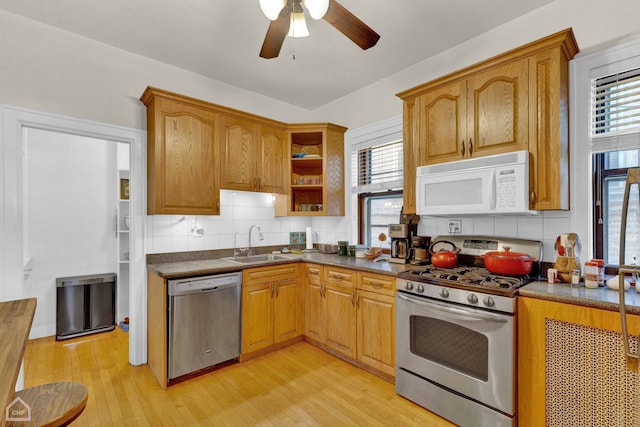 kitchen with dark countertops, backsplash, appliances with stainless steel finishes, a sink, and light wood-type flooring