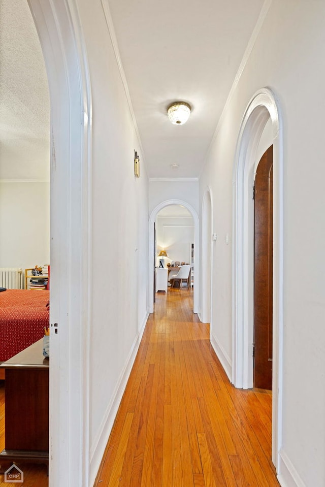 hall with arched walkways, ornamental molding, light wood-style flooring, and baseboards