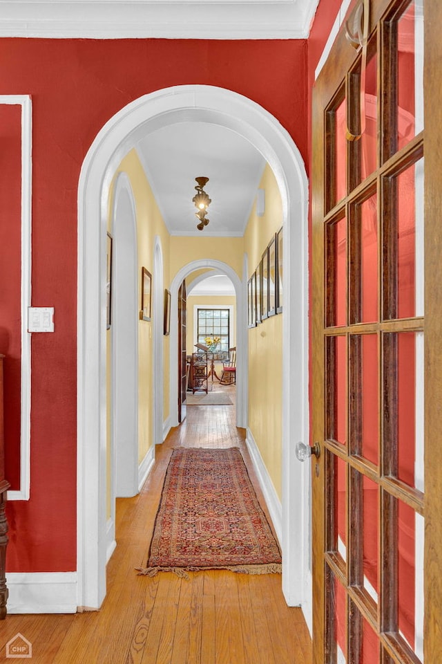 hallway featuring baseboards, hardwood / wood-style flooring, and crown molding