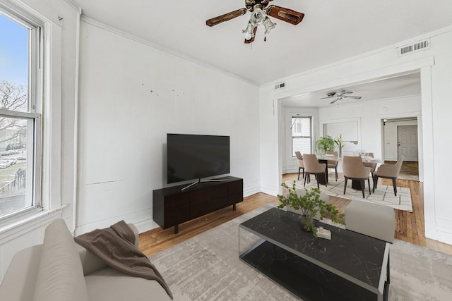 living area with crown molding, light wood-type flooring, visible vents, and ceiling fan