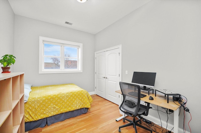 bedroom with a closet, wood finished floors, visible vents, and baseboards