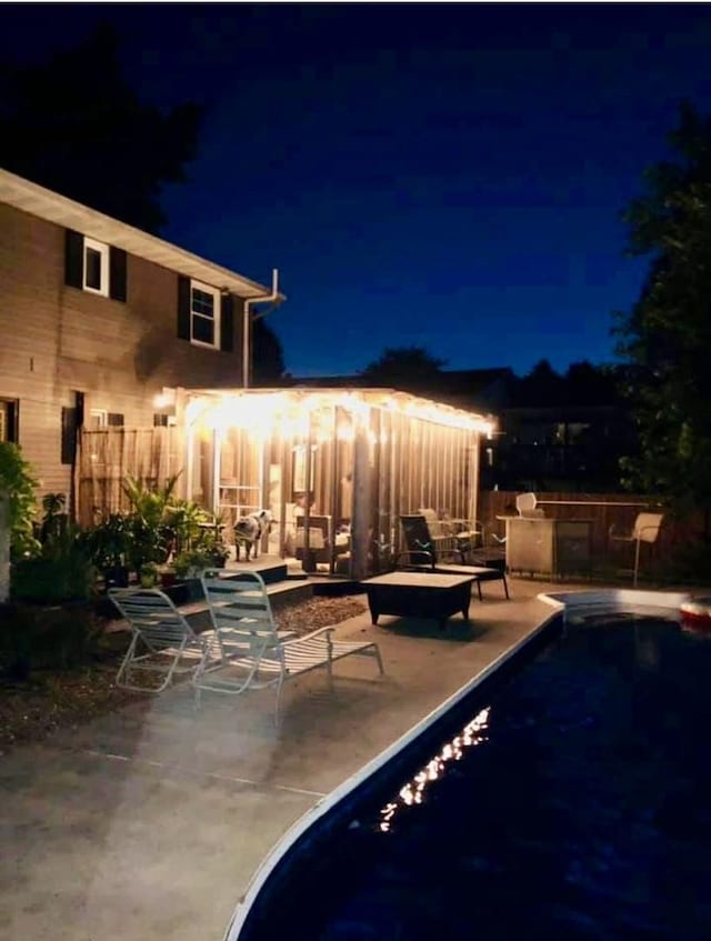 pool at twilight with a patio, fence, and an outdoor pool