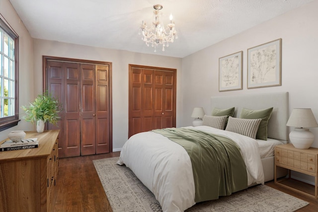 bedroom featuring a notable chandelier, dark wood-style floors, and multiple closets