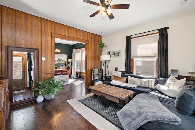 living room featuring dark wood-style floors, wooden walls, and a ceiling fan