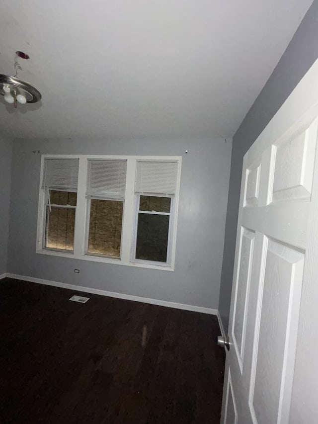 spare room with dark wood-style flooring, visible vents, and baseboards