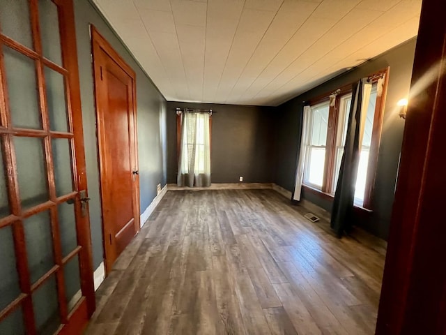 unfurnished room featuring dark wood-type flooring, visible vents, and baseboards