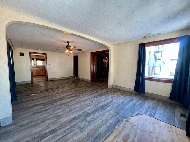 unfurnished room featuring arched walkways, visible vents, ceiling fan, wood finished floors, and baseboards