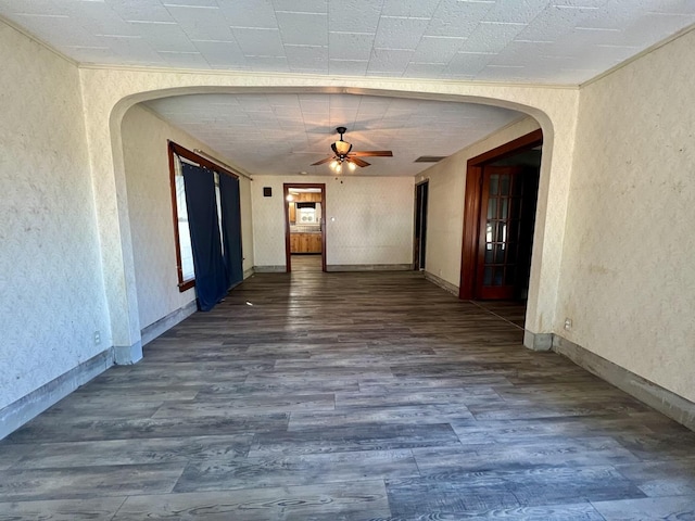 interior space featuring a ceiling fan, arched walkways, baseboards, and wood finished floors