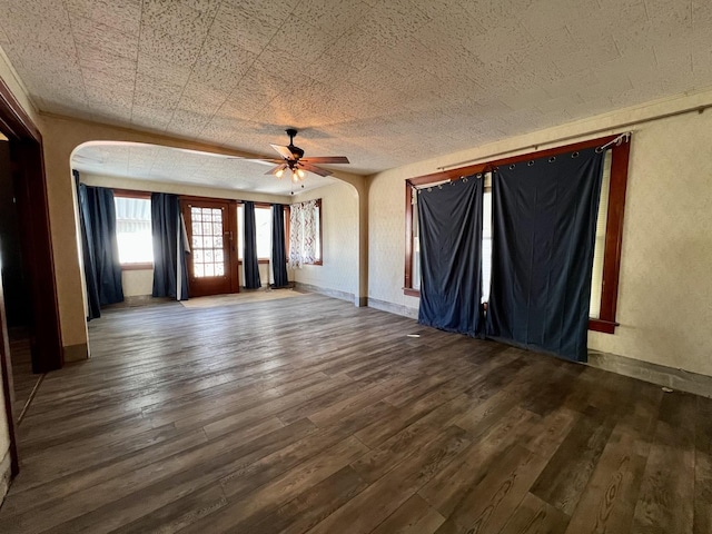 unfurnished living room with arched walkways, wood finished floors, a ceiling fan, and baseboards