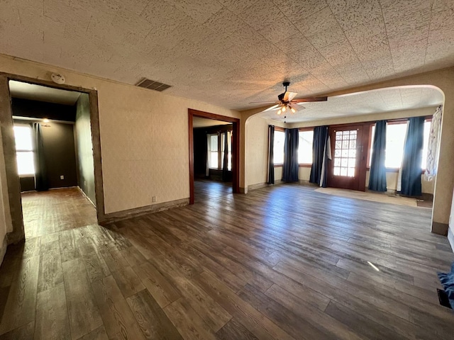 unfurnished living room with baseboards, visible vents, arched walkways, a ceiling fan, and dark wood-style floors