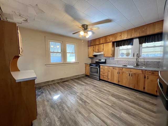 kitchen featuring decorative backsplash, brown cabinets, stainless steel gas range, light wood-style floors, and a sink