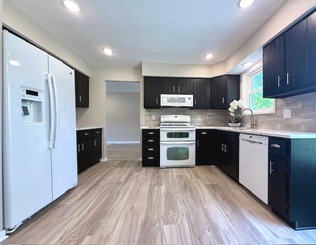 1816 Sadler Dr, Champaign, IL 61821 - kitchen featuring white appliances, dark cabinets, light countertops, a sink, and decorative backsplash