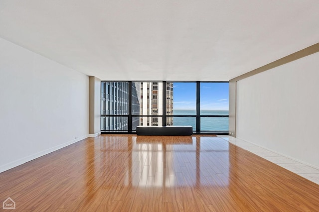 empty room with a water view, light wood-style flooring, baseboards, and a wall of windows