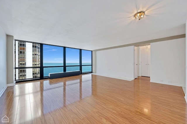 spare room featuring expansive windows, light wood-type flooring, a water view, and baseboards