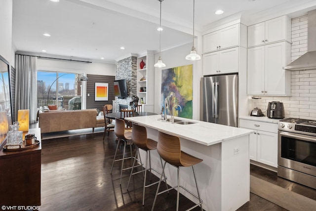 kitchen with dark wood-style flooring, a sink, open floor plan, appliances with stainless steel finishes, and wall chimney range hood