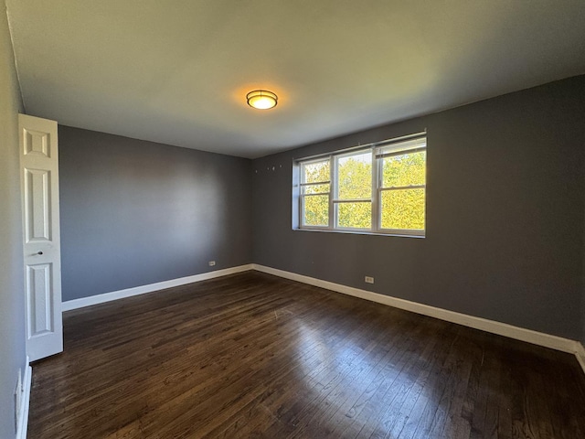 spare room featuring dark wood-style flooring and baseboards