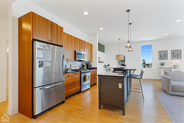 kitchen featuring stainless steel appliances, dark countertops, hanging light fixtures, a kitchen island with sink, and a kitchen breakfast bar