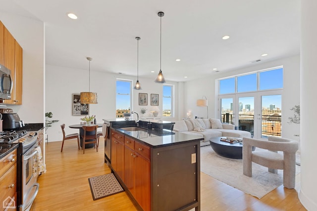 kitchen with brown cabinets, stainless steel appliances, dark countertops, hanging light fixtures, and a kitchen island with sink