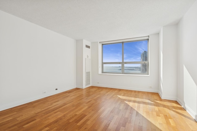 empty room with baseboards, a textured ceiling, visible vents, and light wood-style floors