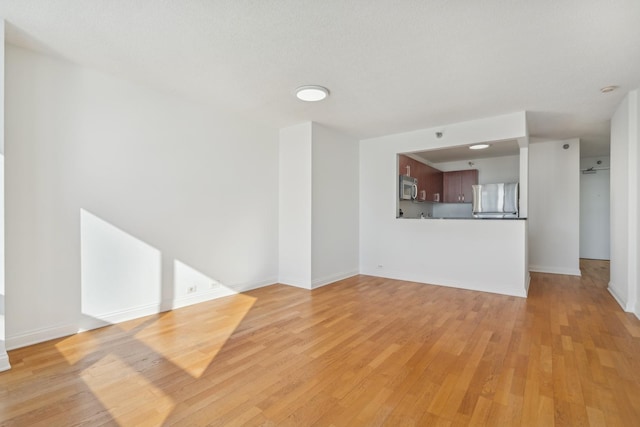 unfurnished living room with light wood-type flooring and baseboards