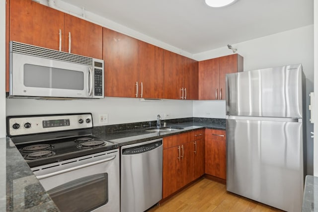 kitchen with a sink, appliances with stainless steel finishes, brown cabinets, dark stone counters, and light wood finished floors