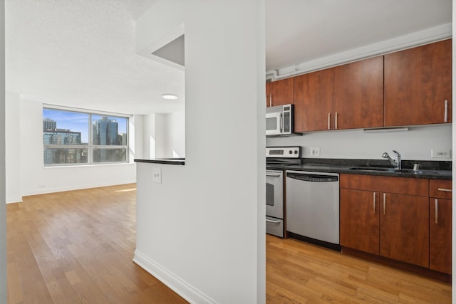 kitchen with stainless steel appliances, dark stone countertops, a sink, and light wood finished floors