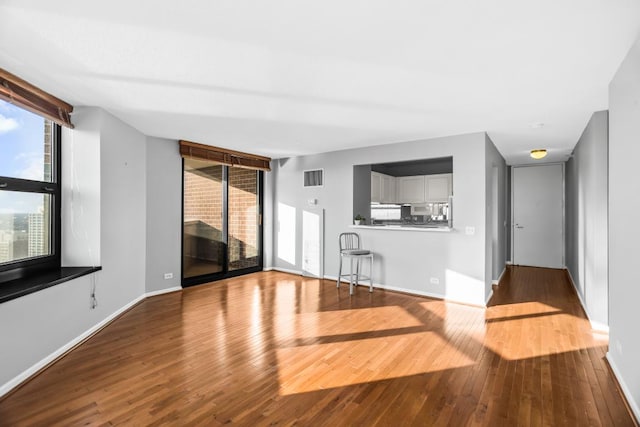 unfurnished living room with wood-type flooring, visible vents, and baseboards