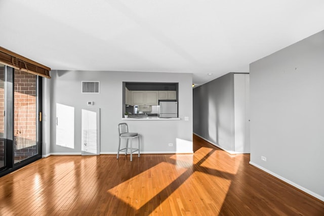 unfurnished living room featuring expansive windows, wood-type flooring, visible vents, and baseboards