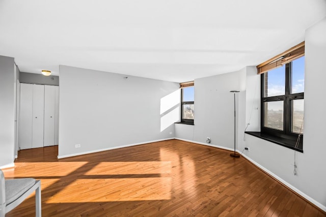 empty room with a wealth of natural light, wood-type flooring, and baseboards