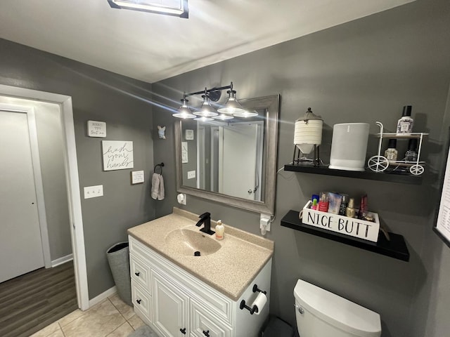 half bathroom with toilet, tile patterned flooring, baseboards, and vanity