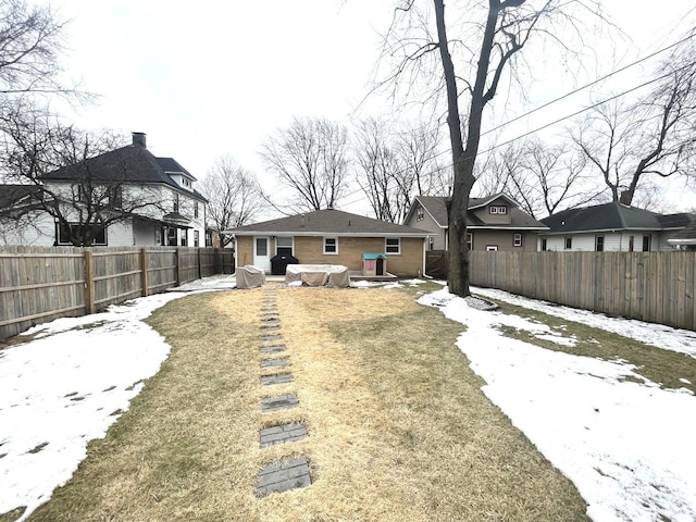 snow covered house featuring a yard, brick siding, and a fenced backyard