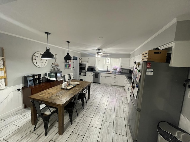 dining room with a wainscoted wall, wood tiled floor, a ceiling fan, and crown molding