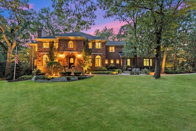 back of house at dusk featuring a chimney, a lawn, and brick siding