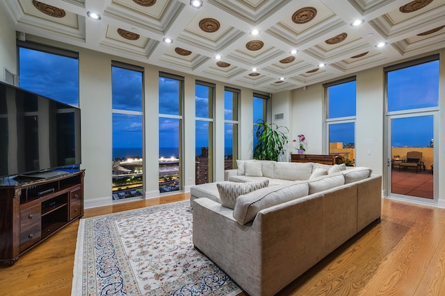 living room featuring light wood-type flooring, coffered ceiling, crown molding, and a high ceiling