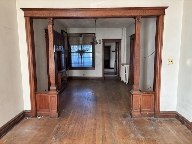 interior space featuring baseboards, radiator heating unit, decorative columns, and dark wood-type flooring