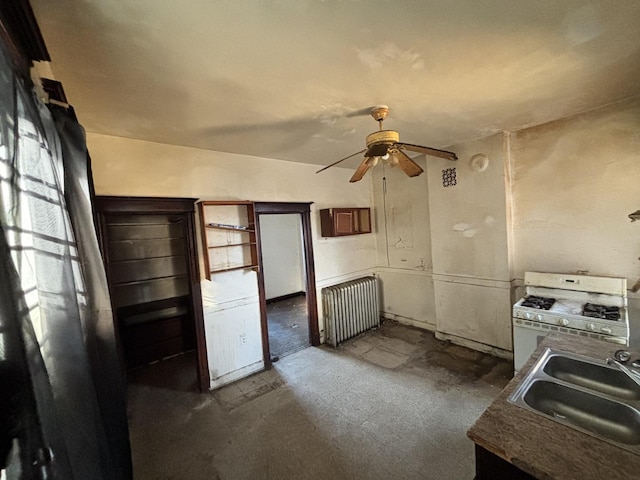 kitchen featuring radiator heating unit, white range with gas cooktop, ceiling fan, and a sink