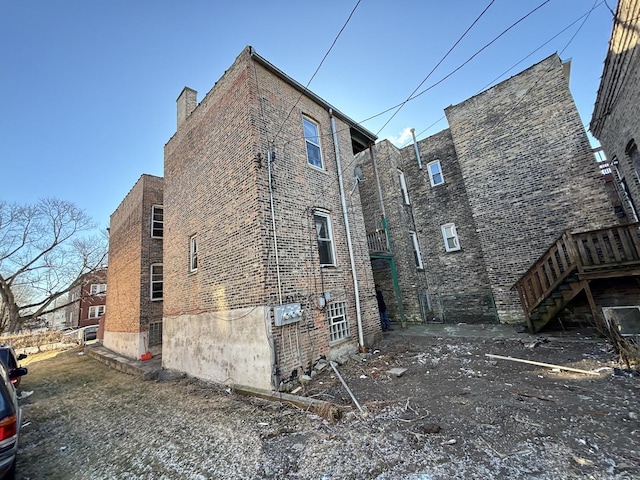 view of side of home with a chimney, brick siding, and stairway