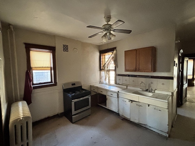 kitchen with radiator, a healthy amount of sunlight, stainless steel gas range oven, and brown cabinets