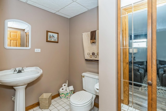 bathroom with baseboards, a drop ceiling, toilet, and tile patterned floors