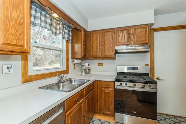 kitchen featuring under cabinet range hood, stainless steel appliances, a sink, light countertops, and brown cabinetry