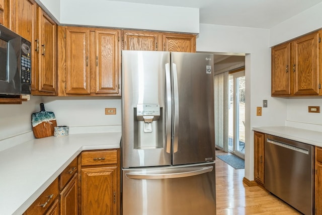 kitchen with stainless steel appliances, light wood-type flooring, brown cabinetry, and light countertops