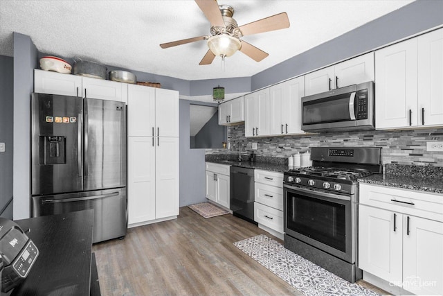 kitchen with dark wood-style floors, white cabinetry, appliances with stainless steel finishes, decorative backsplash, and dark stone counters