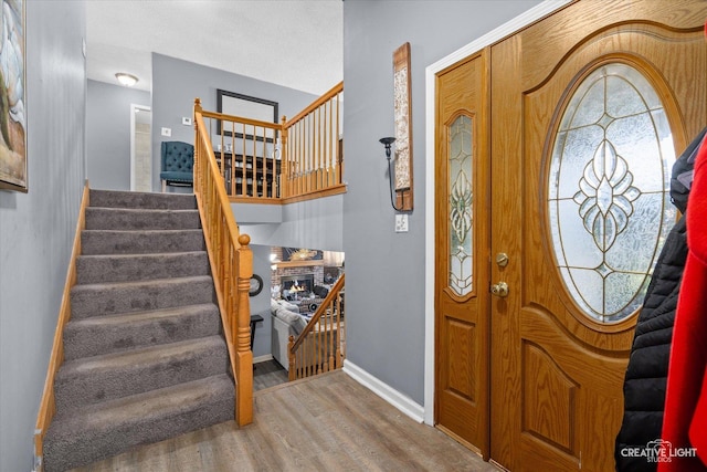 entrance foyer with stairs, a brick fireplace, baseboards, and wood finished floors