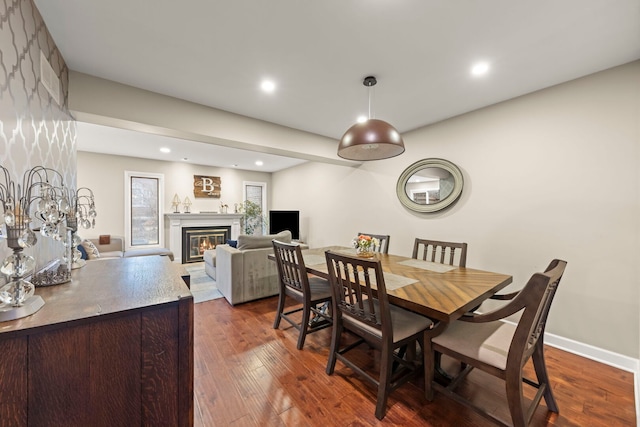 dining space featuring a glass covered fireplace, dark wood finished floors, baseboards, and recessed lighting