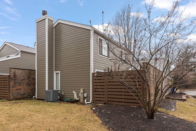 view of side of home featuring a chimney, a lawn, and cooling unit