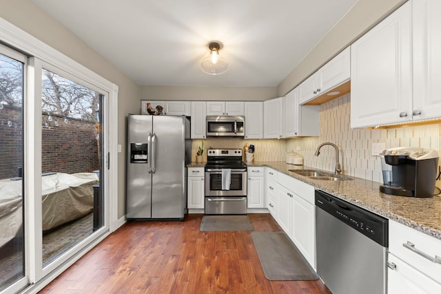 kitchen featuring stainless steel appliances, backsplash, dark wood-type flooring, a sink, and light stone countertops